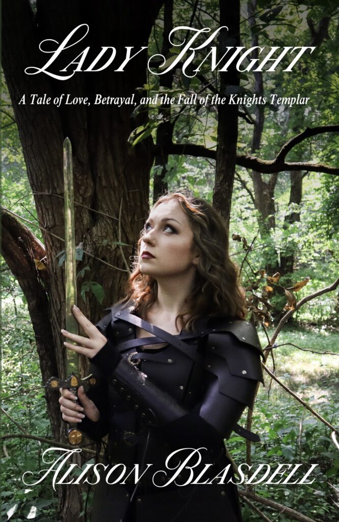 A woman in medieval armor stands in a forest, holding a sword and gazing thoughtfully, embodying the theme of bravery in "Lady Knight."